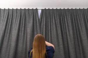 A young girl closes heavy gray curtains on the window in a hotel room