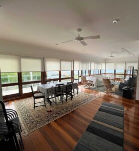 Bright living room with large windows, roller blinds, and wooden floors, featuring a dining area and cozy seating arrangement.