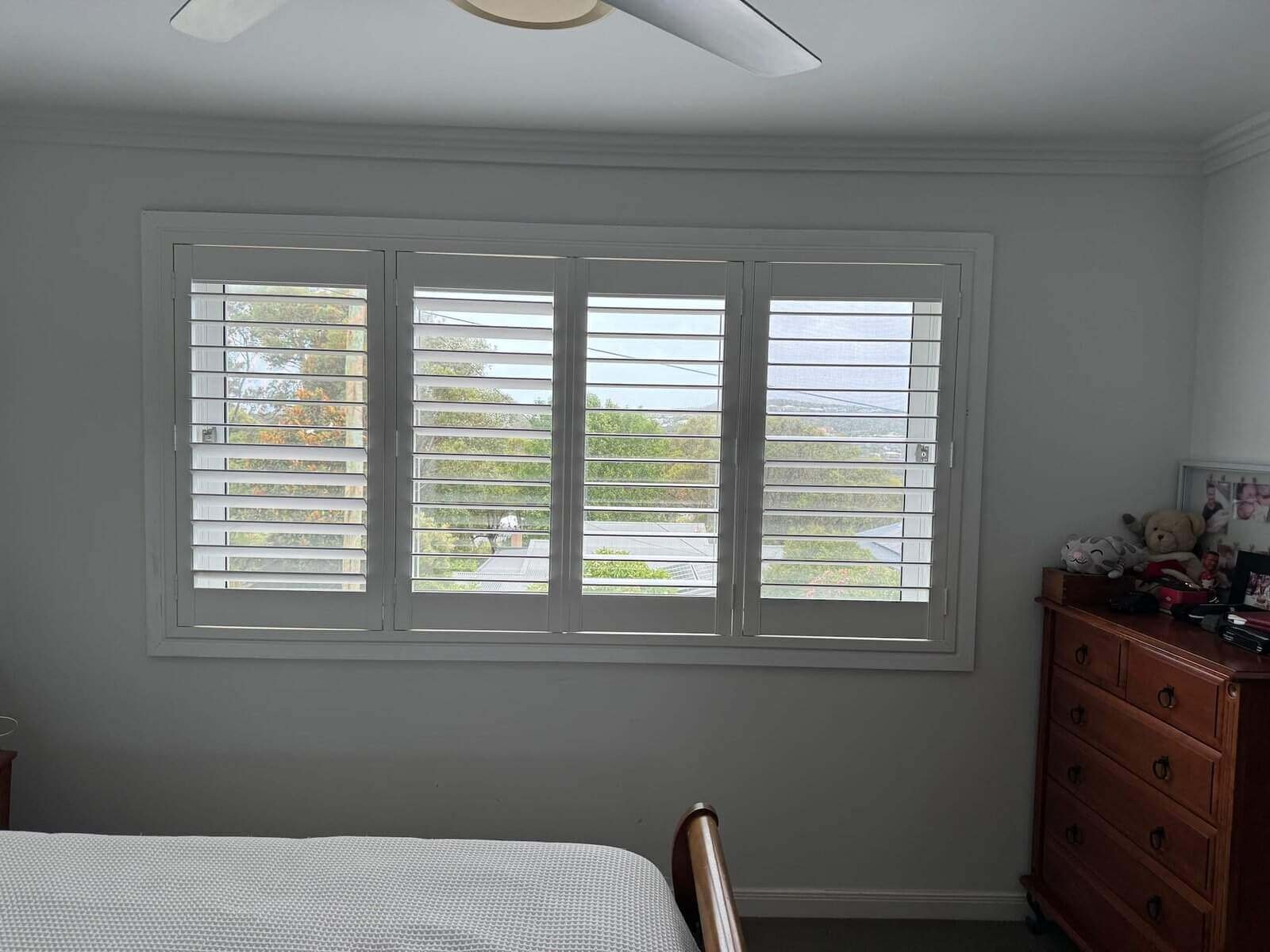 White PVC plantation shutters installed in a bright coastal bedroom – are-pvc-shutters-better-than-wood comparison image.